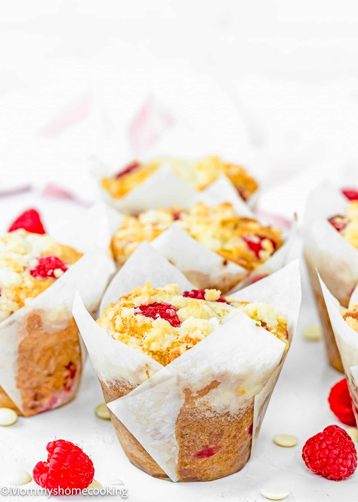 Easy Vegan Raspberry Muffins with tulip liners over a white surface with fresh raspberries and white chocolate around them.