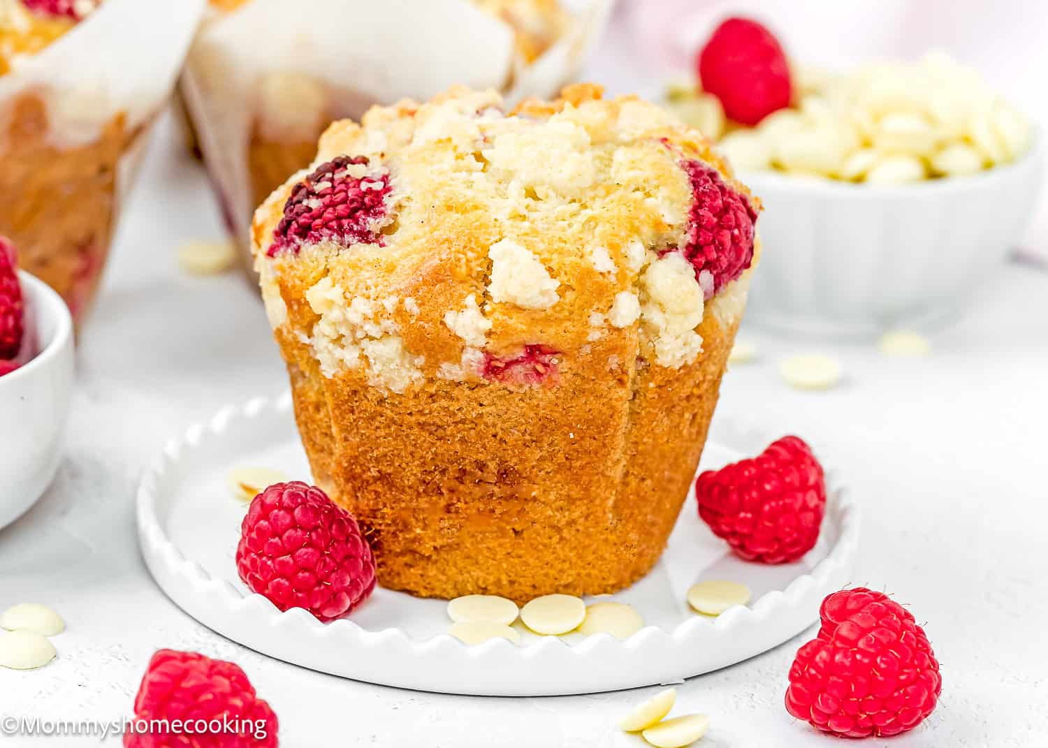 a Easy Vegan Raspberry Muffin on a little white plate with fresh raspberries and white chocolate around it with.