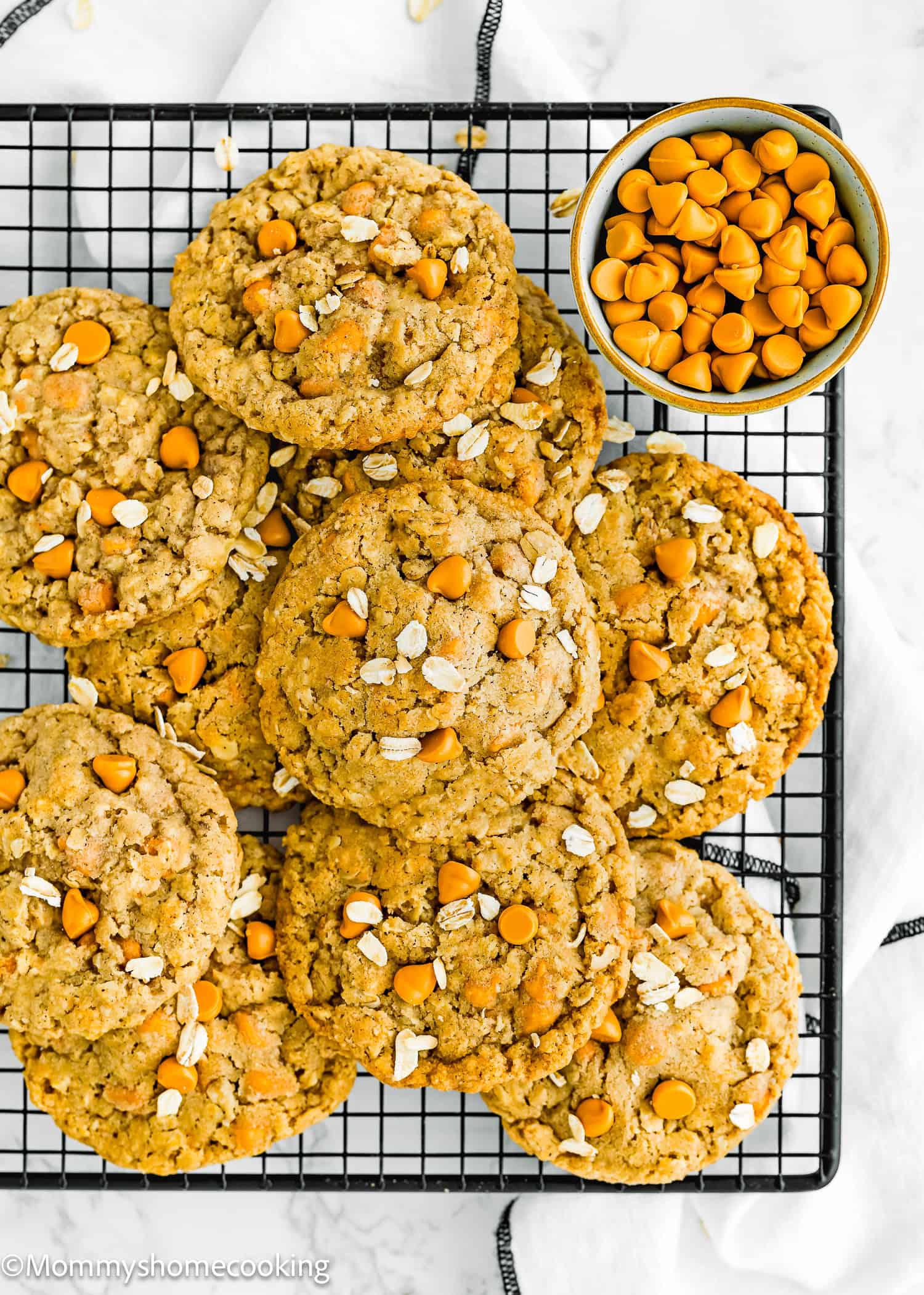 Eggless Easy Oatmeal Scotchies Cookies over a cooling rack with a bowl with butterscotch chips on the side over a marble surface.