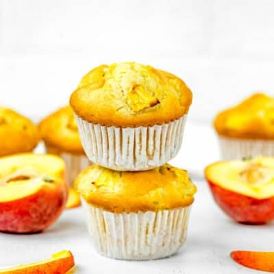 stack of two Vegan Easy Peach Muffins made without eggs and dairy over a white surface with fresh peaches on the side.