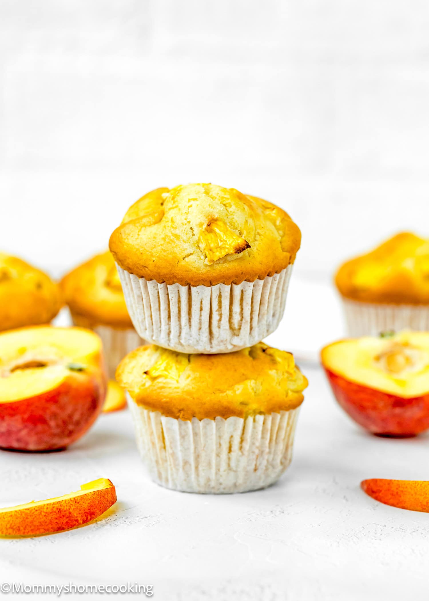 stack of two Vegan Easy Peach Muffins made without eggs and dairy over a white surface with fresh peaches on the side.