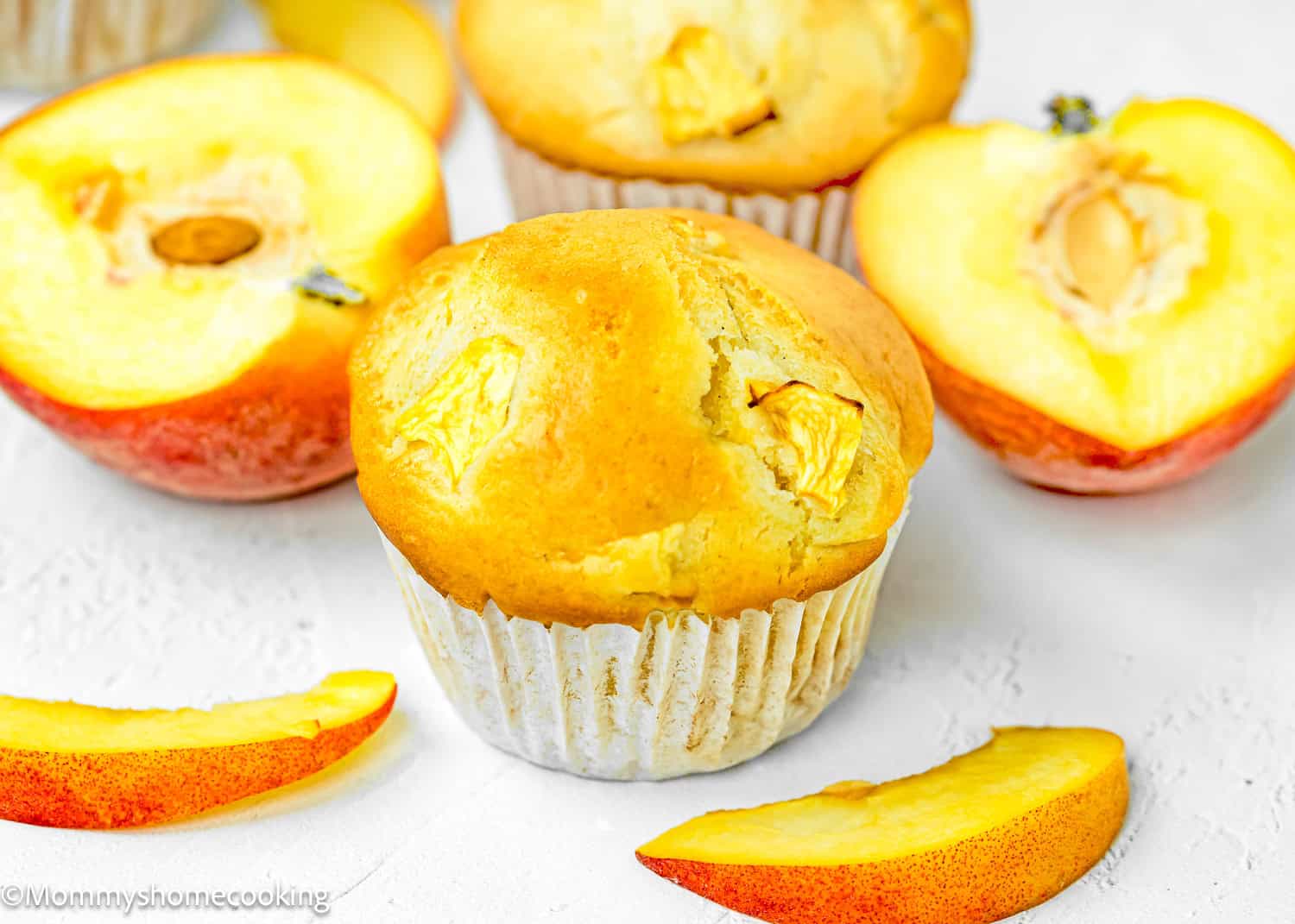 a Easy Peach Muffin made without eggs and dairy over a white surface with fresh peaches on the side.