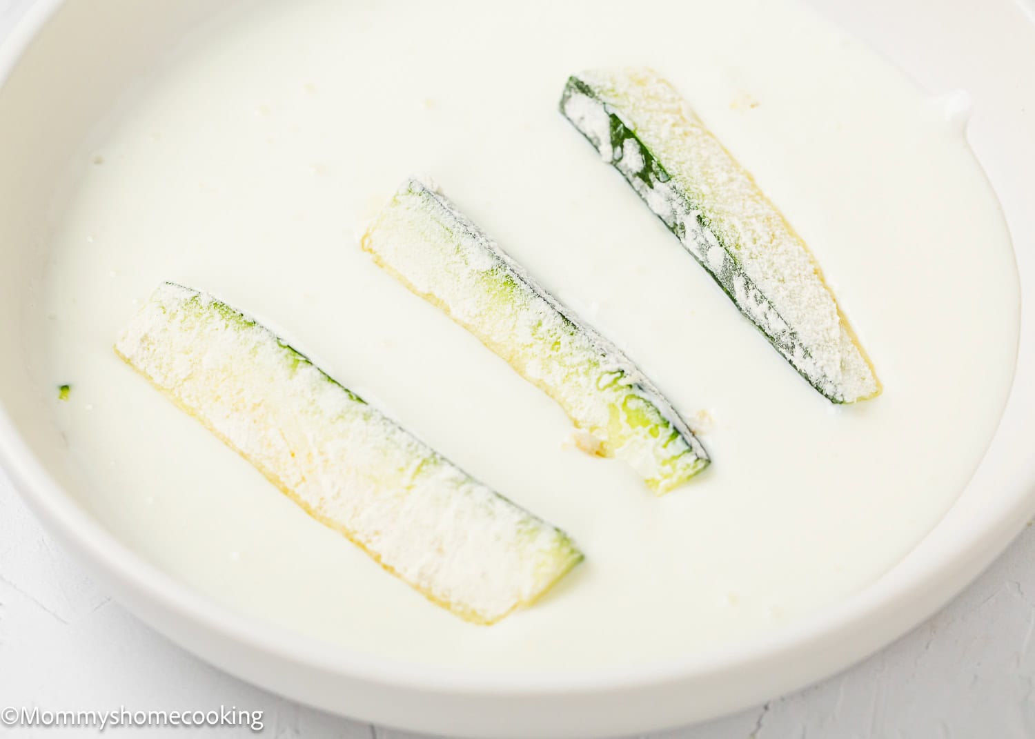 Zucchini sticks dipped in a yogurt mixture to make Eggless Zucchini Fries in a bowl.