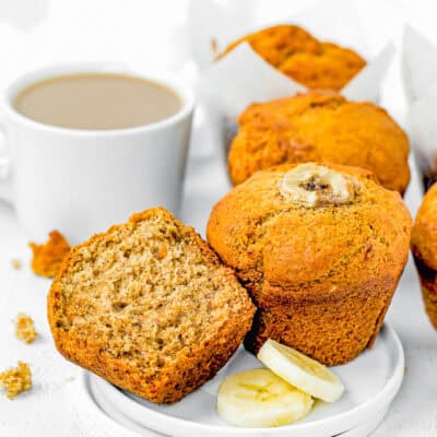 Healthy Easy Banana Muffins made with no eggs, dairy or sugar in a small plate with more muffins and a cup of coffee in the background.