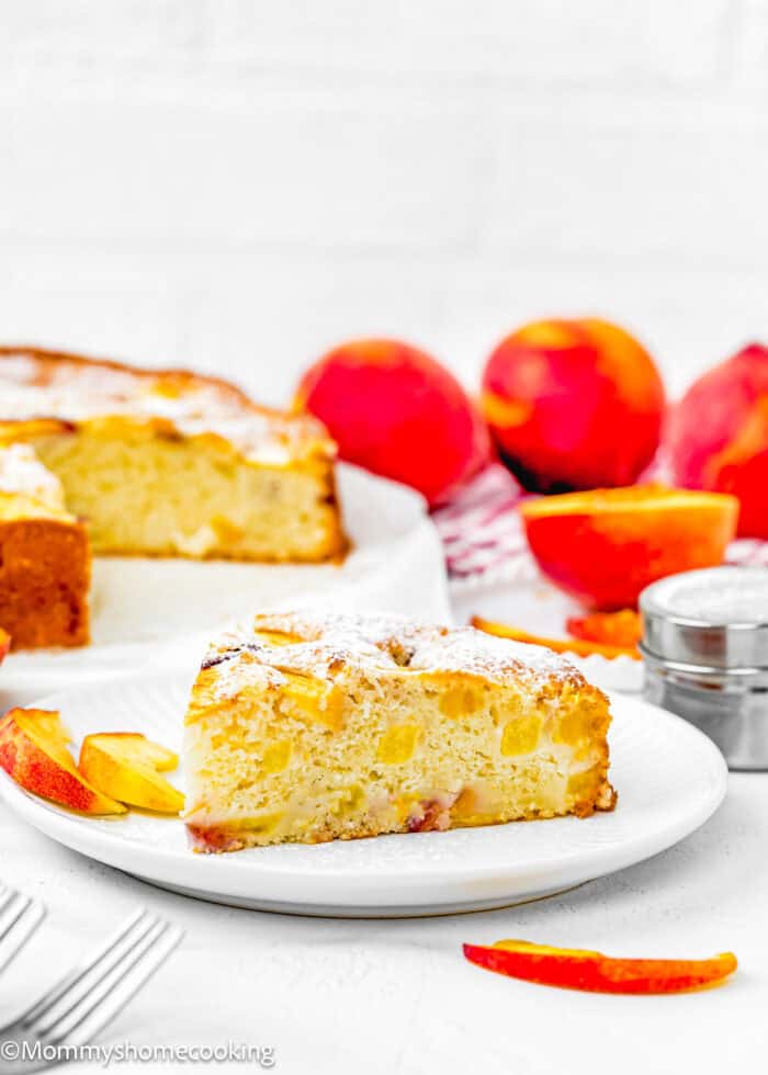 slice of Easy Peach Cake made without eggs and dairy over a plate with a fork and the whole cake on the background.