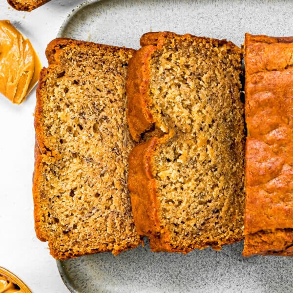 sliced Vegan Peanut Butter Banana Bread over a gray serving plate and a bowl and spatula with peanut butter.