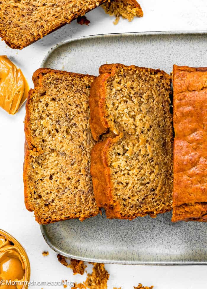 sliced Vegan Peanut Butter Banana Bread over a gray serving plate and a bowl and spatula with peanut butter.
