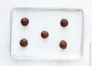Five chocolate dough balls for the Best Eggless Brownie Cookies are spaced on a parchment-lined baking sheet, ready to be baked.
