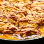 Easy Caramel Peach Cobbler in a skillet drizzled with caramel sauce over a dark surface.