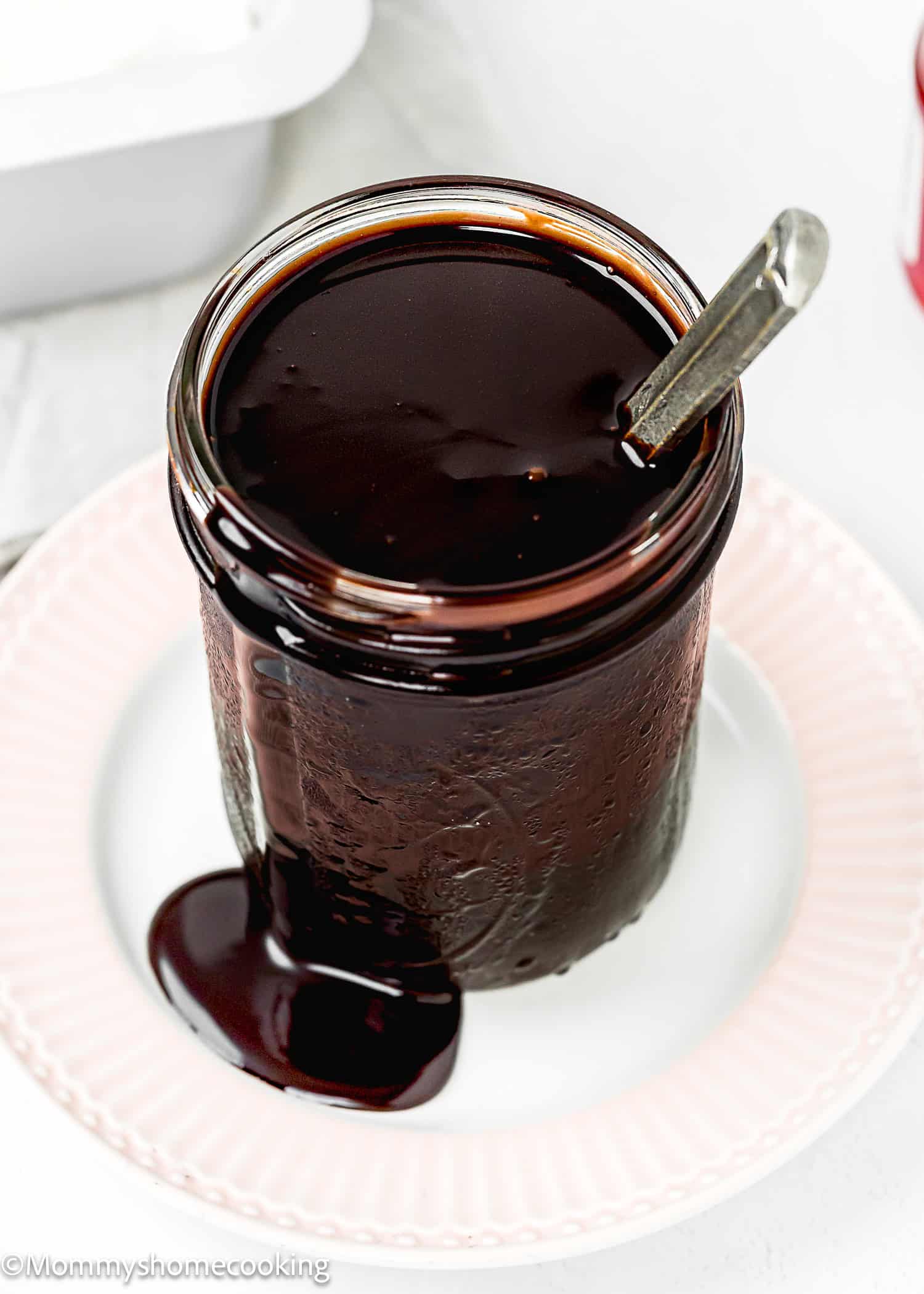 homemade Chocolate Hot Fudge Sauce in a jar over a plate with a spoon.