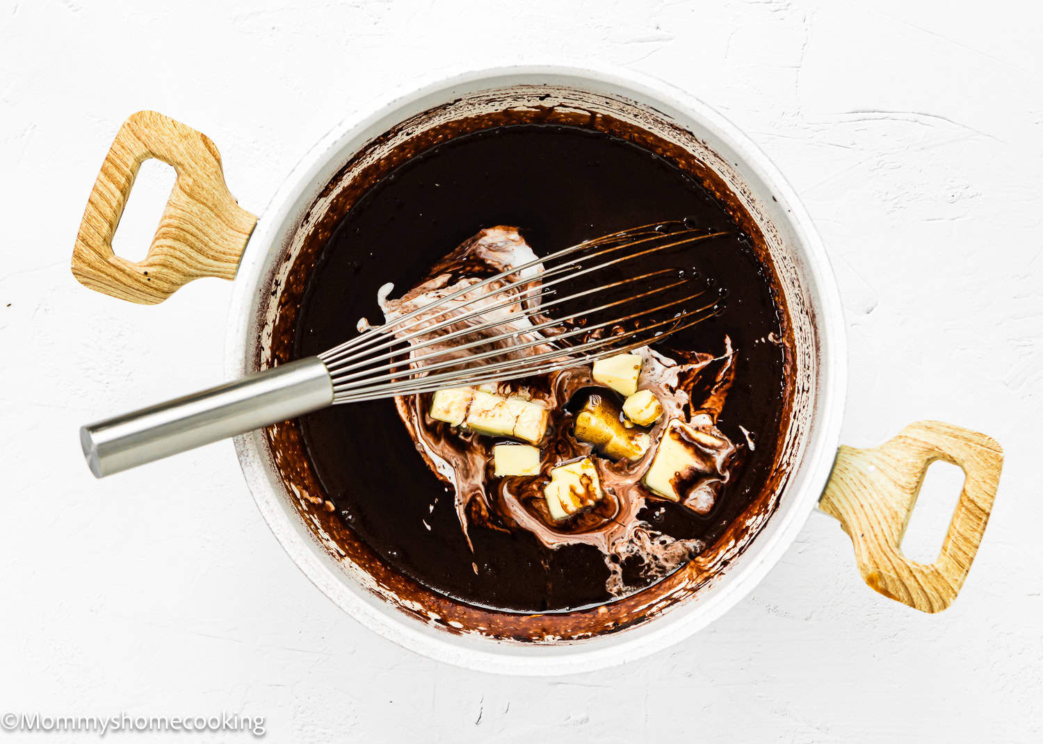 homemade Chocolate Hot Fudge Sauce in a pot with butter and a whisk.