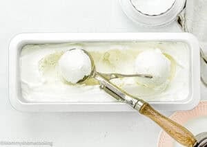 Eggless Vanilla Ice Cream in a loaf mold with a ice cream scoop in it.