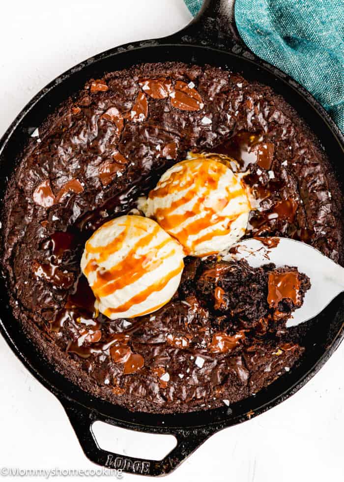 baked Easy Skillet Brownie made without eggs with salt flakes on top with ice cream on top and a serving spoon.