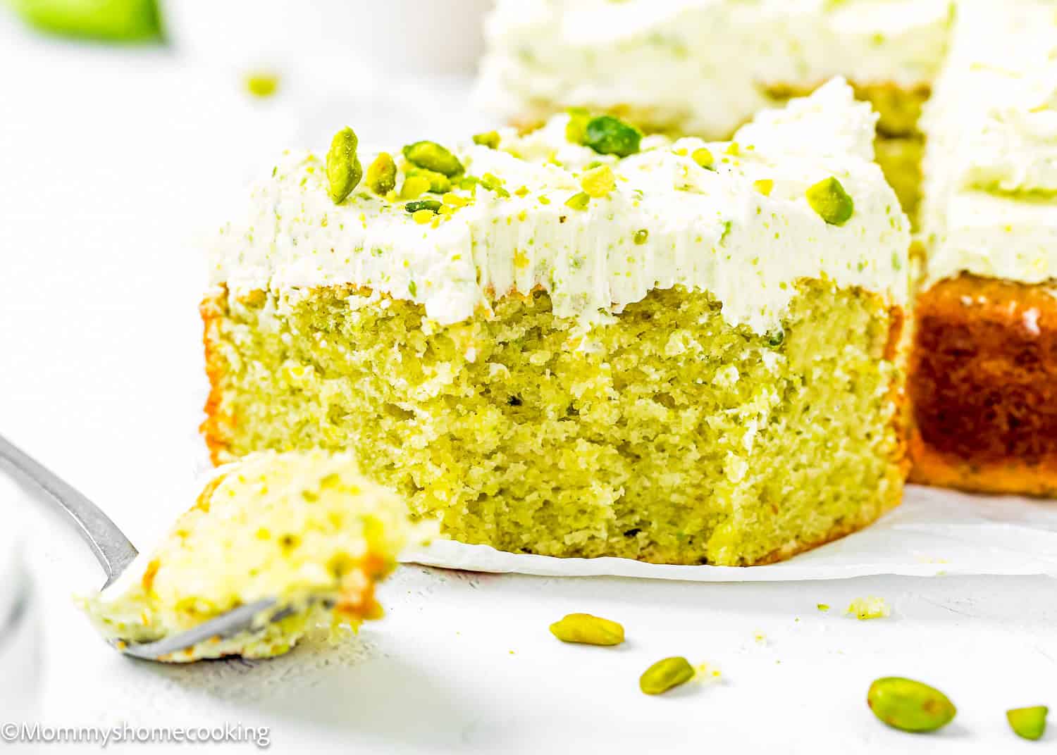 slice of Easy Pistachio Cake showing its perfect fluffy inside texture over a piece of parchment paper.