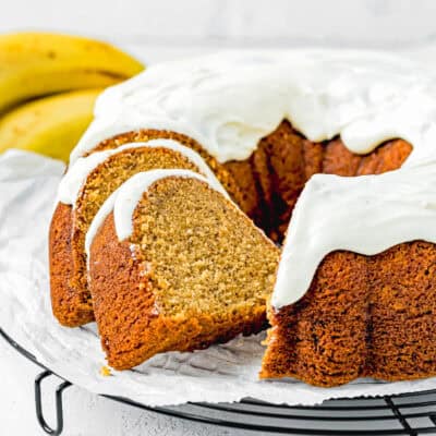 sliced Egg-free Brown Butter Banana Bundt Cake with glaze over a cooling rack with fresh bananas on the side.