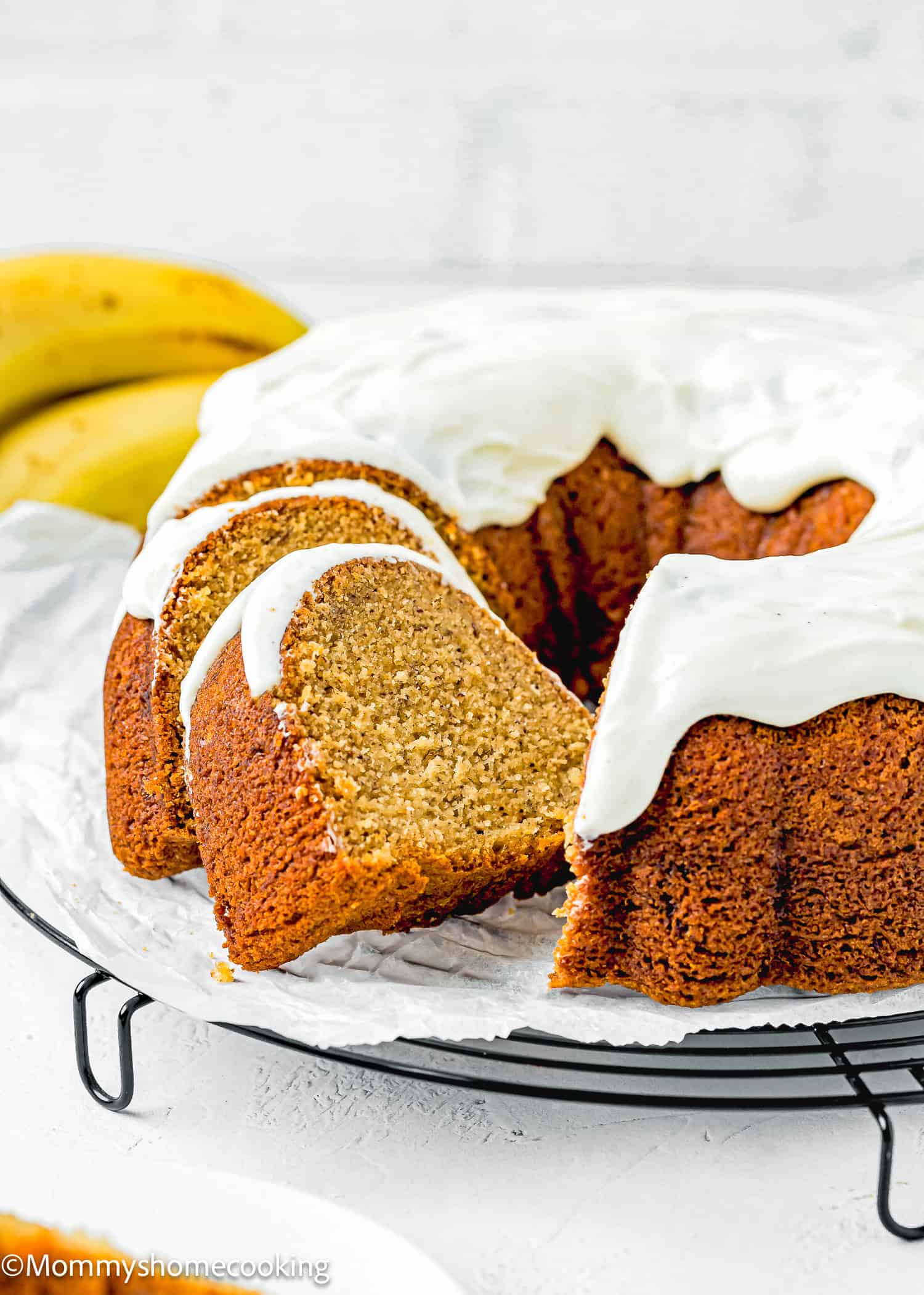 sliced Egg-free Brown Butter Banana Bundt Cake with glaze over a cooling rack with fresh bananas on the side.