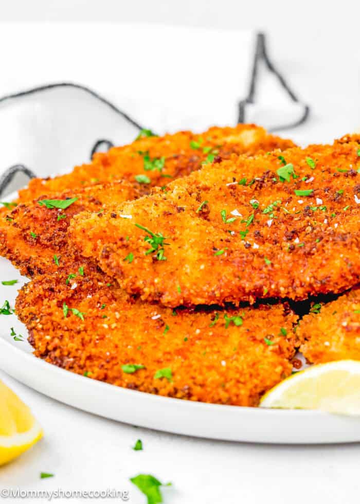Eggless Chicken Cutlets on a plate garnished with sea salt flakes, chopped fresh parsley and lemon wedges.