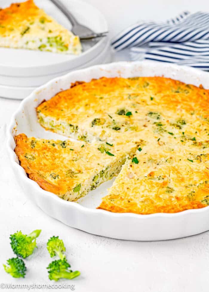sliced Egg-Free Crustless Quiche in a quiche dish over a white surface with plates, forks and a kitchen towel on the side.