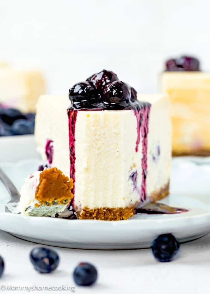 Eggless Easy Blueberry Cheesecake slide on blue plate with blueberry sauce on top and a fork on the side.