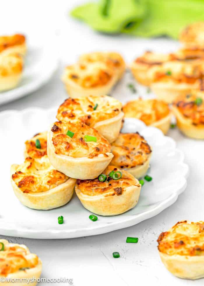 Eggless Easy Mini Quiches on a plate with more mini quiches on the sides over a white surface.