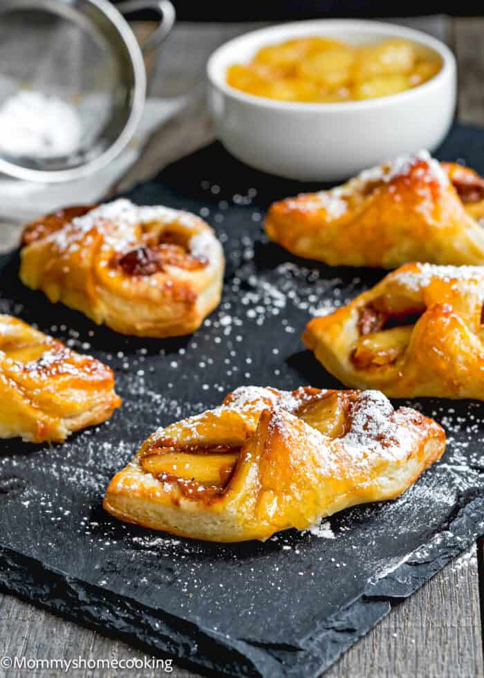 Eggless Apple and Dulce de Leche Puffs over a black surface with a bowl with glazed apples on the background.