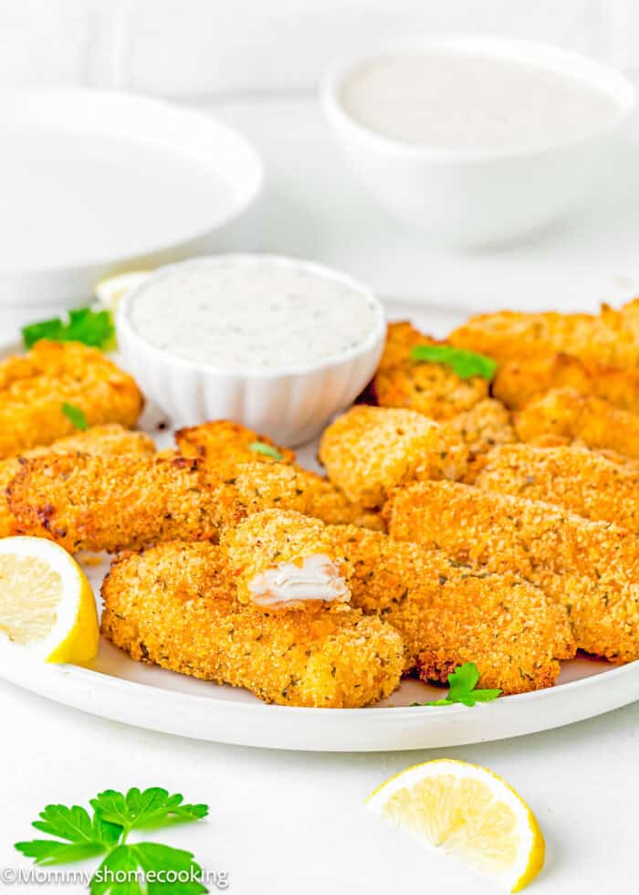 Easy homemade Fish Sticks made without eggs and vegan tartar sauce in a plate with lemon wedges.