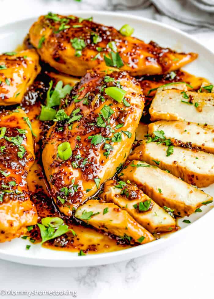 Easy Mustard Glazed Chicken with sauce and chopped parsley and green onions on a plate over a marble surface with a kitchen towel on the background.