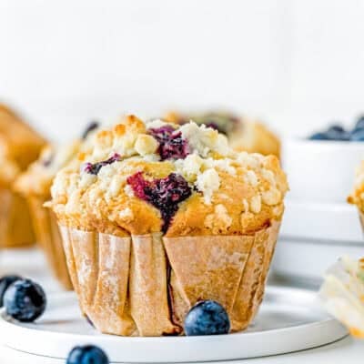 a egg-free, dairy-free, Vegan Blueberry Muffin over a plate with fresh blueberries on the sides and muffins in the background.