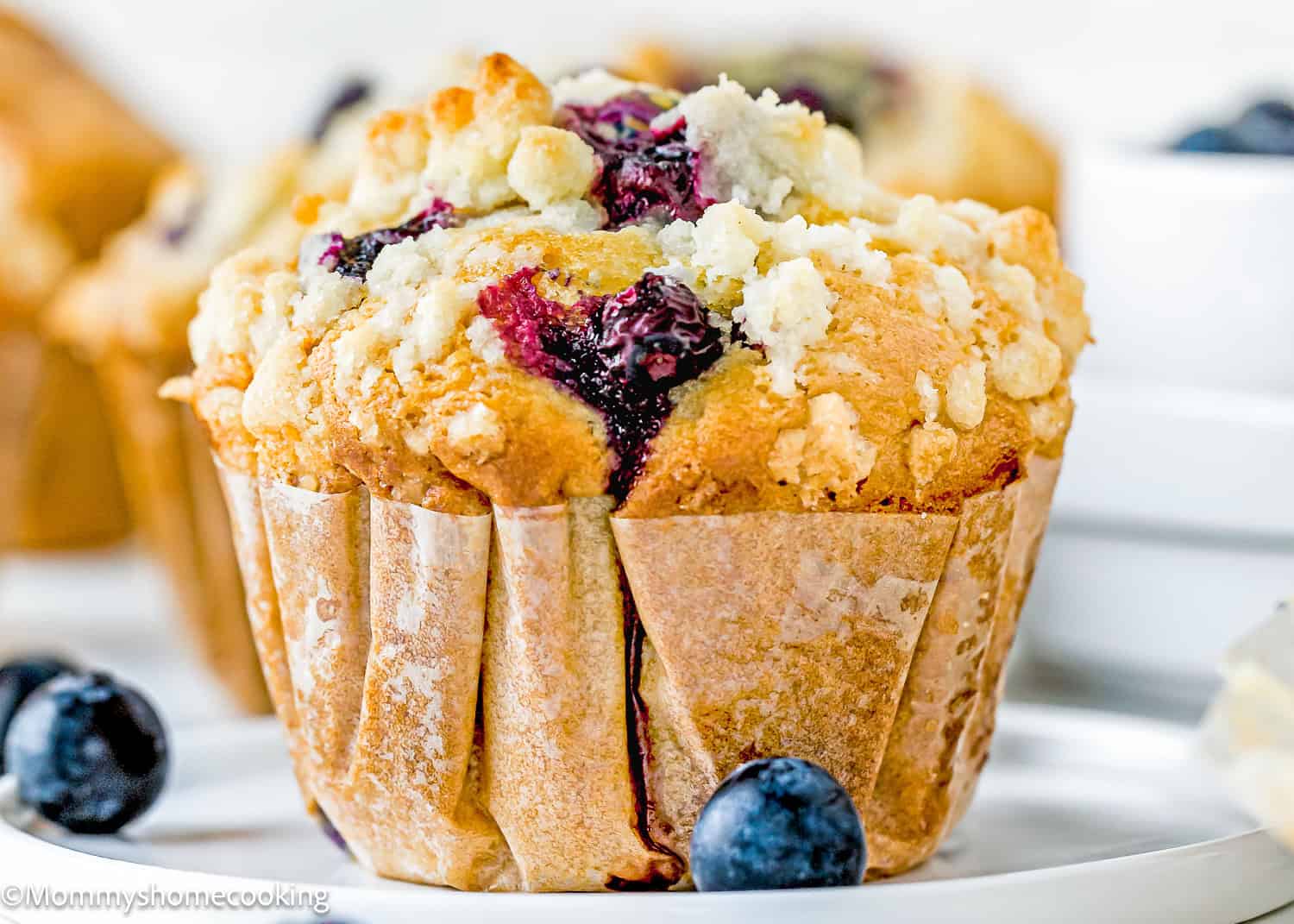 a Vegan Blueberry Muffin over a plate with fresh blueberries on the sides.