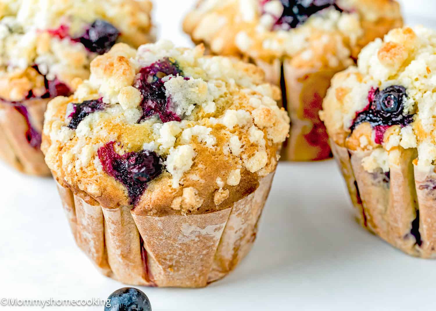 egg-free and dairy-free Blueberry Muffins with crumb on top over a white surface.