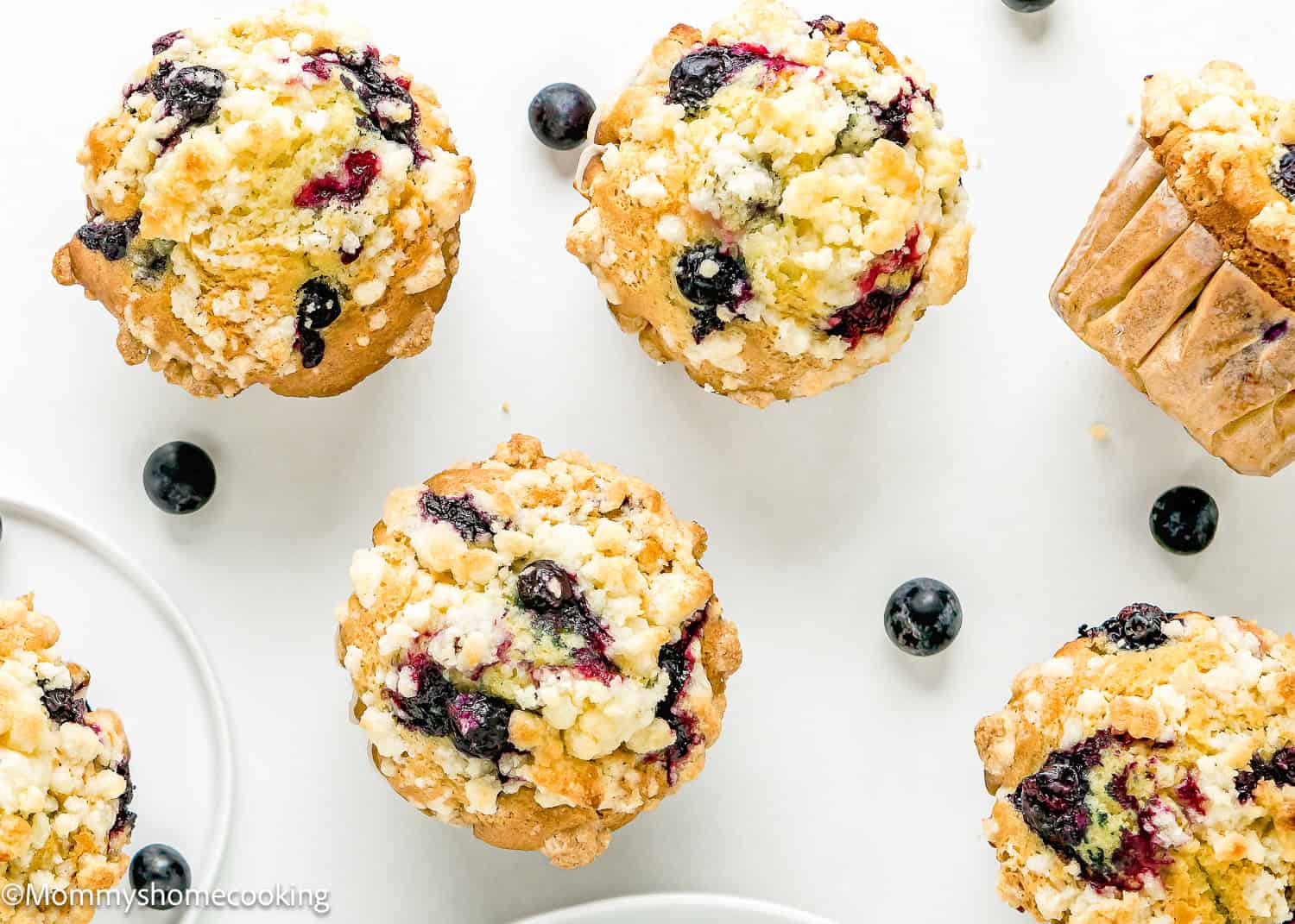 a Vegan Blueberry Muffins over a white surface with fresh blueberries on the sides.