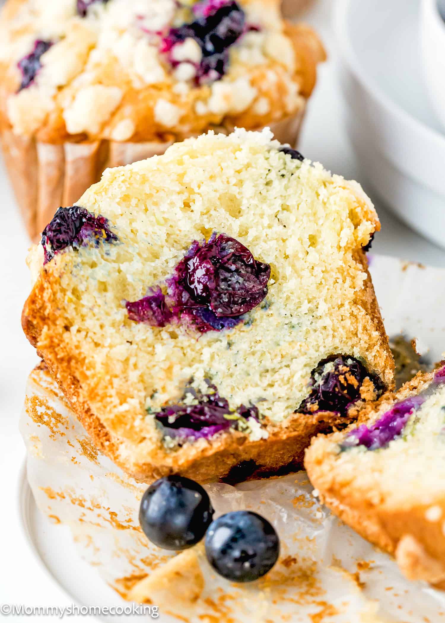 a Vegan Blueberry Muffin cut in half showing its perfect texture over a plate with fresh blueberries on the sides.