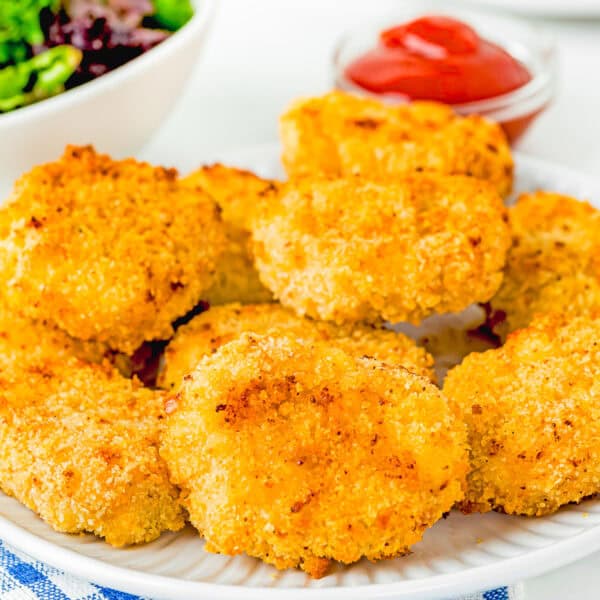 Eggless Homemade Chicken Nuggets on a plate with ketchup and a small bowl with greens and strawberries on the background.