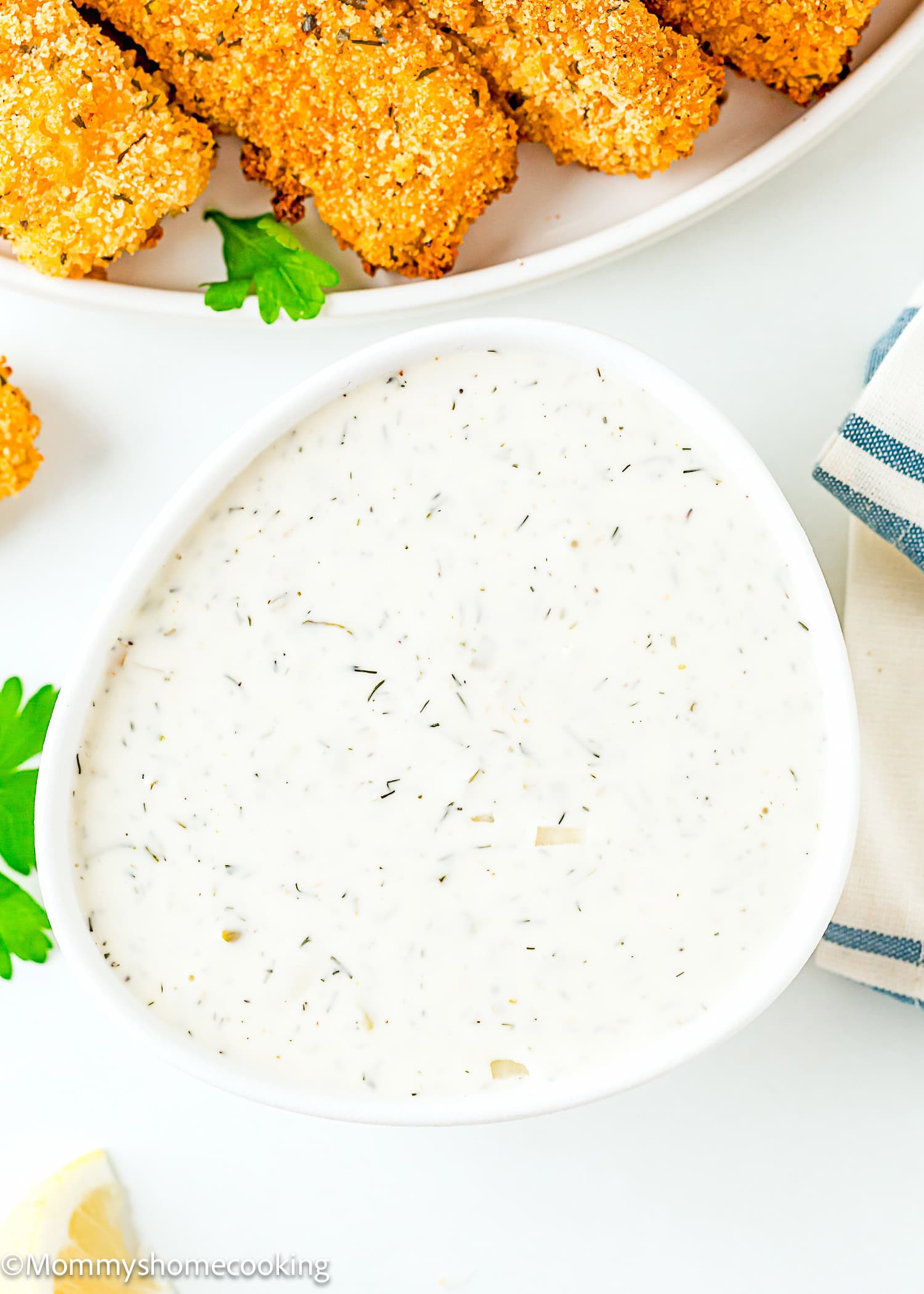 Homemade Easy Vegan Tartar Sauce in a white bowl with fish sticks and a lemon wedge on the side over a white surface.