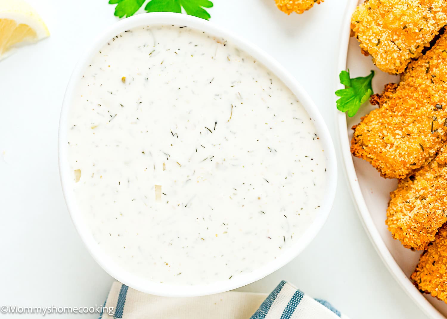 Homemade Easy egg-free Tartar Sauce in a white bowl with fish sticks and a lemon wedge on the side over a white surface.