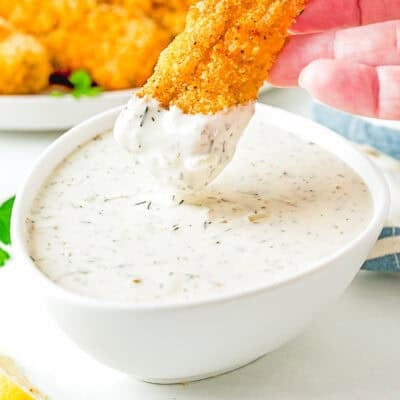 a women hand dipping an egg-free homemade fish stick into a bowl with Homemade Easy Vegan Tartar Sauce.