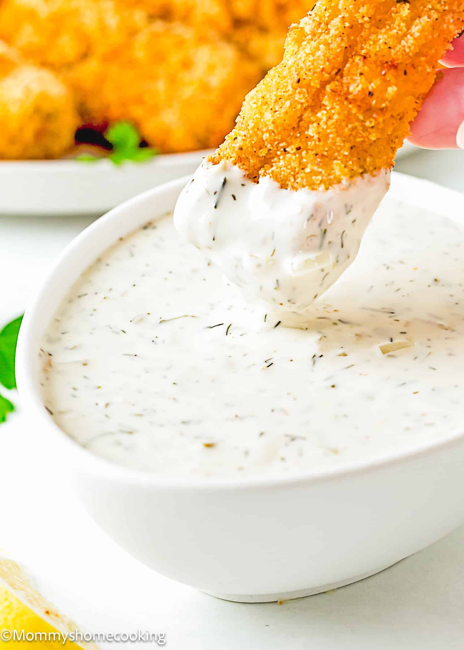 an egg-free homemade fish stick being dipped into a bowl with Homemade Easy Vegan Tartar Sauce.