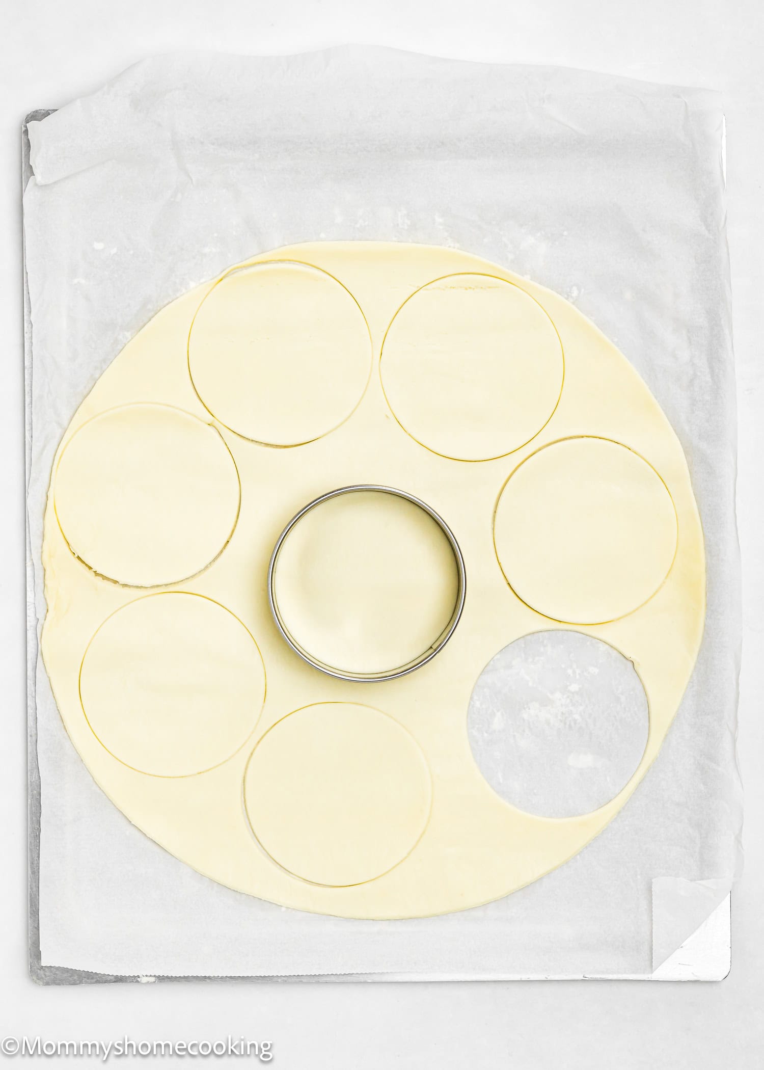 A sheet of dough with round shapes, perfect for crafting eggless mini pumpkin pies, is cut out using a circular cutter and placed gently on parchment paper.