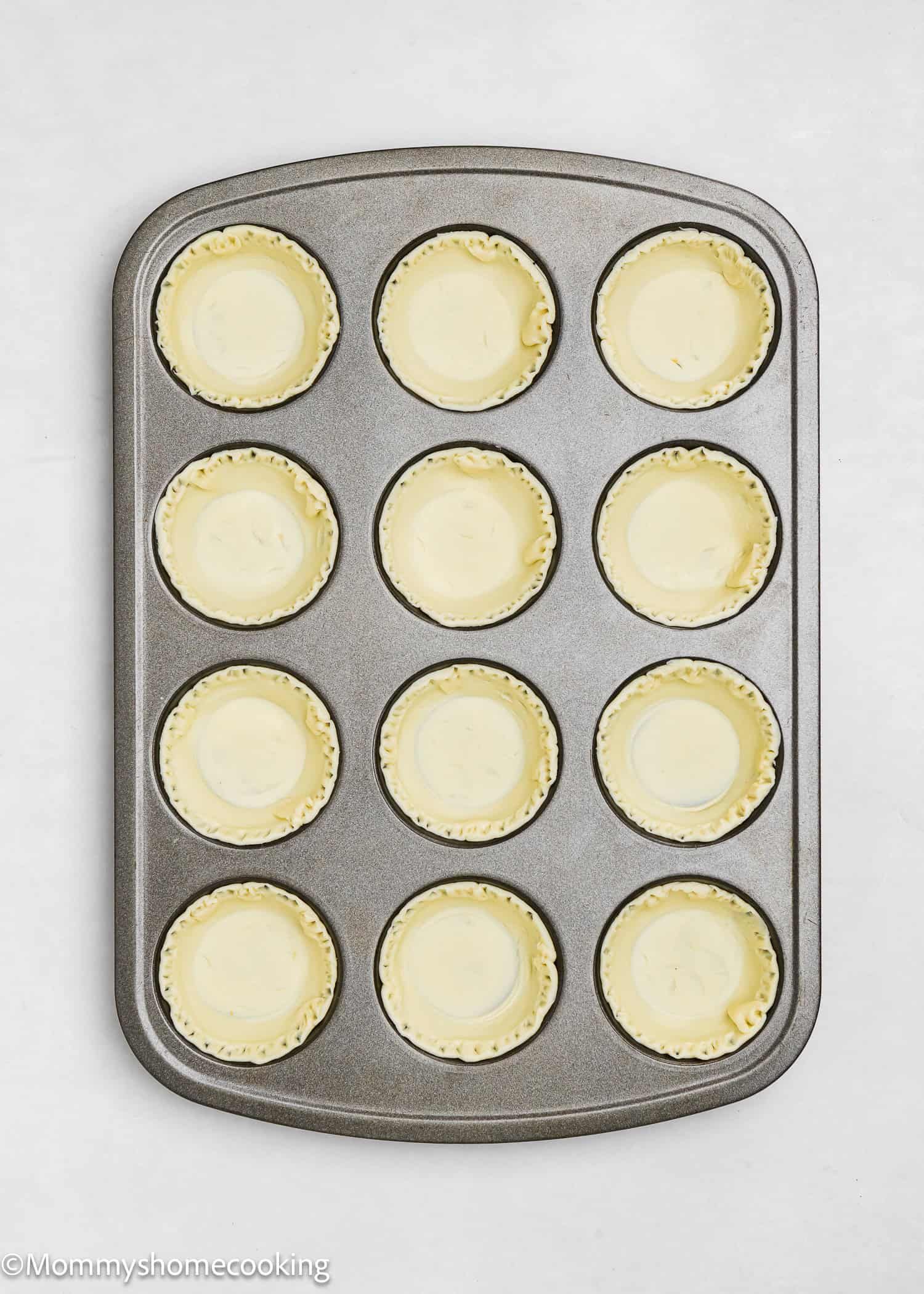 Muffin tin with 12 unbaked pastry shells evenly placed, ready for filling. Perfect for creating delightful eggless mini pumpkin pies.