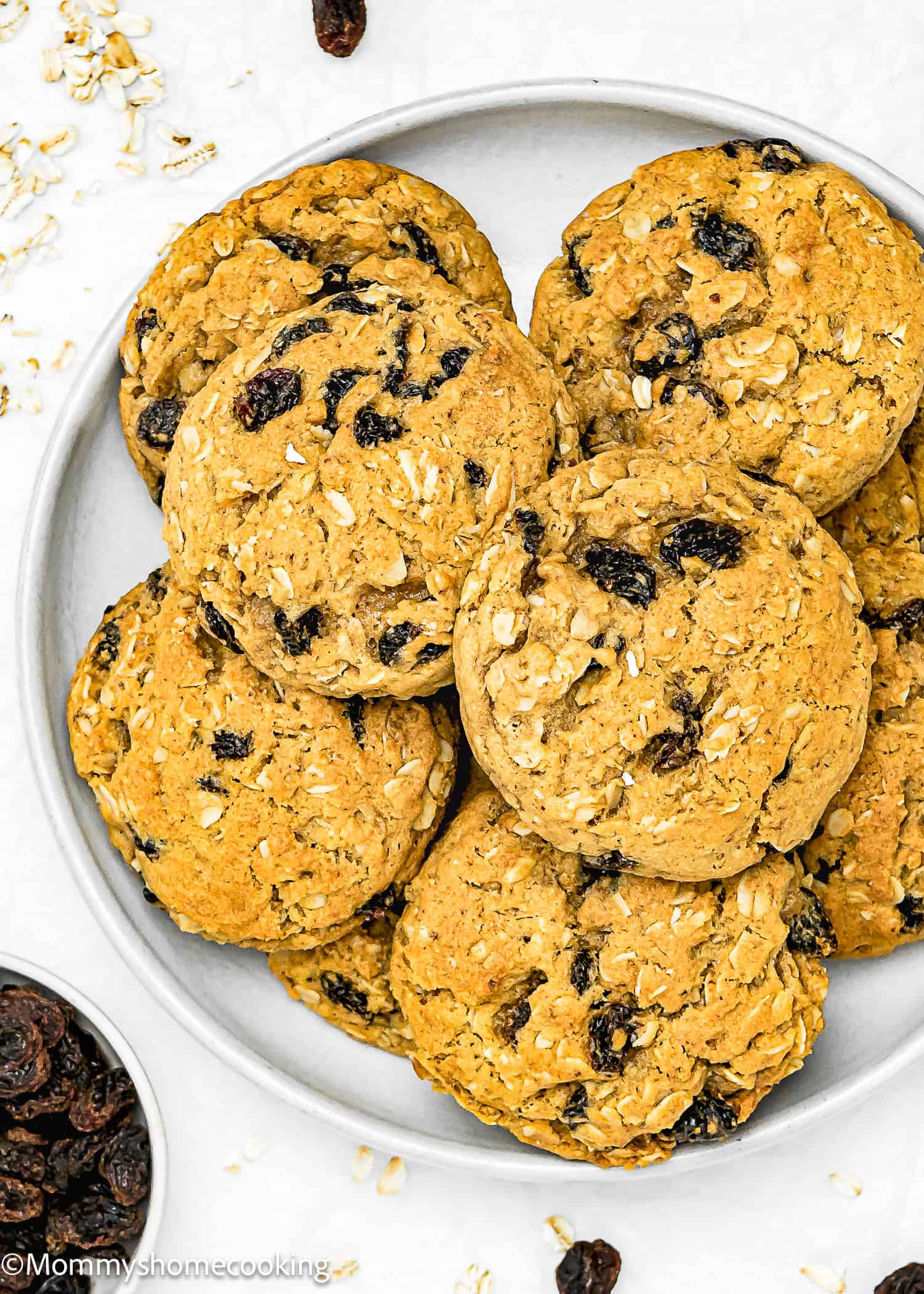 A plate of egg-free oatmeal raisin cookies stacked neatly, with scattered oats and raisins nearby. The one-bowl recipe makes them easy to make and enjoy anytime.