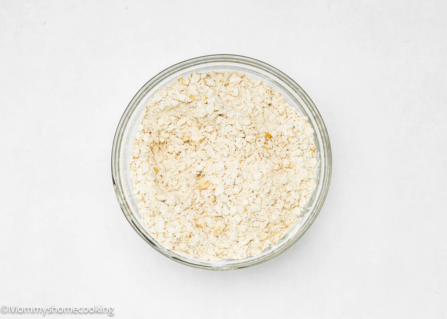 A glass bowl filled with dry ingredients to make eggless oatmeal raisin cookies. 