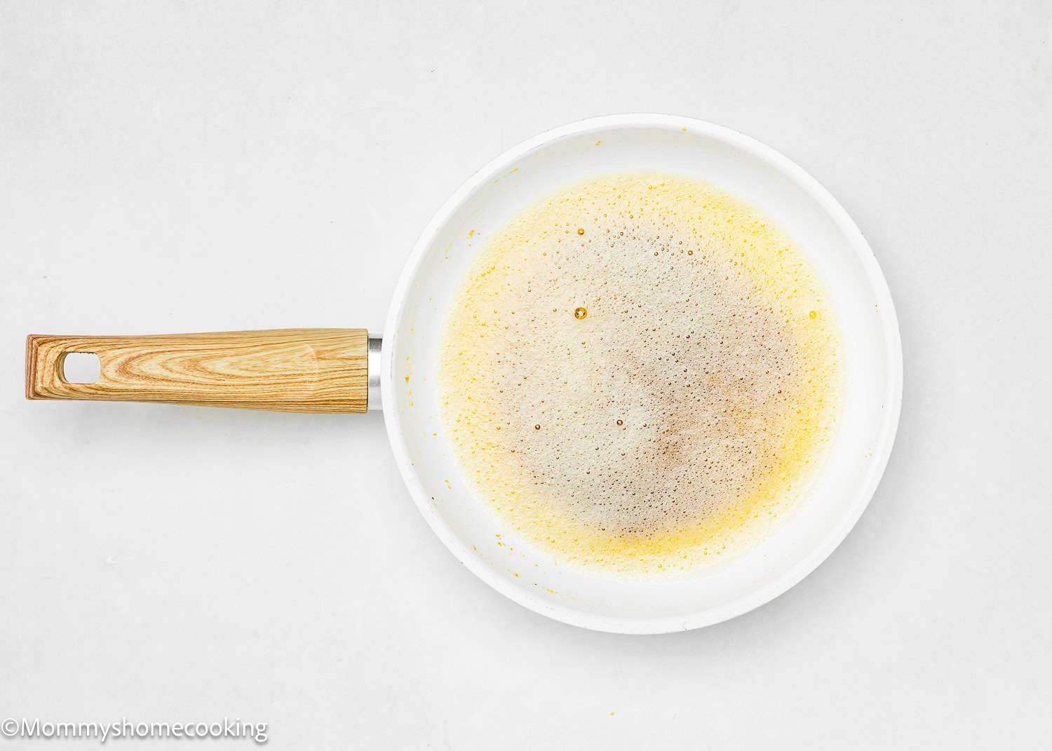 brown butter in a white frying pan with a wooden handle on a white surface.