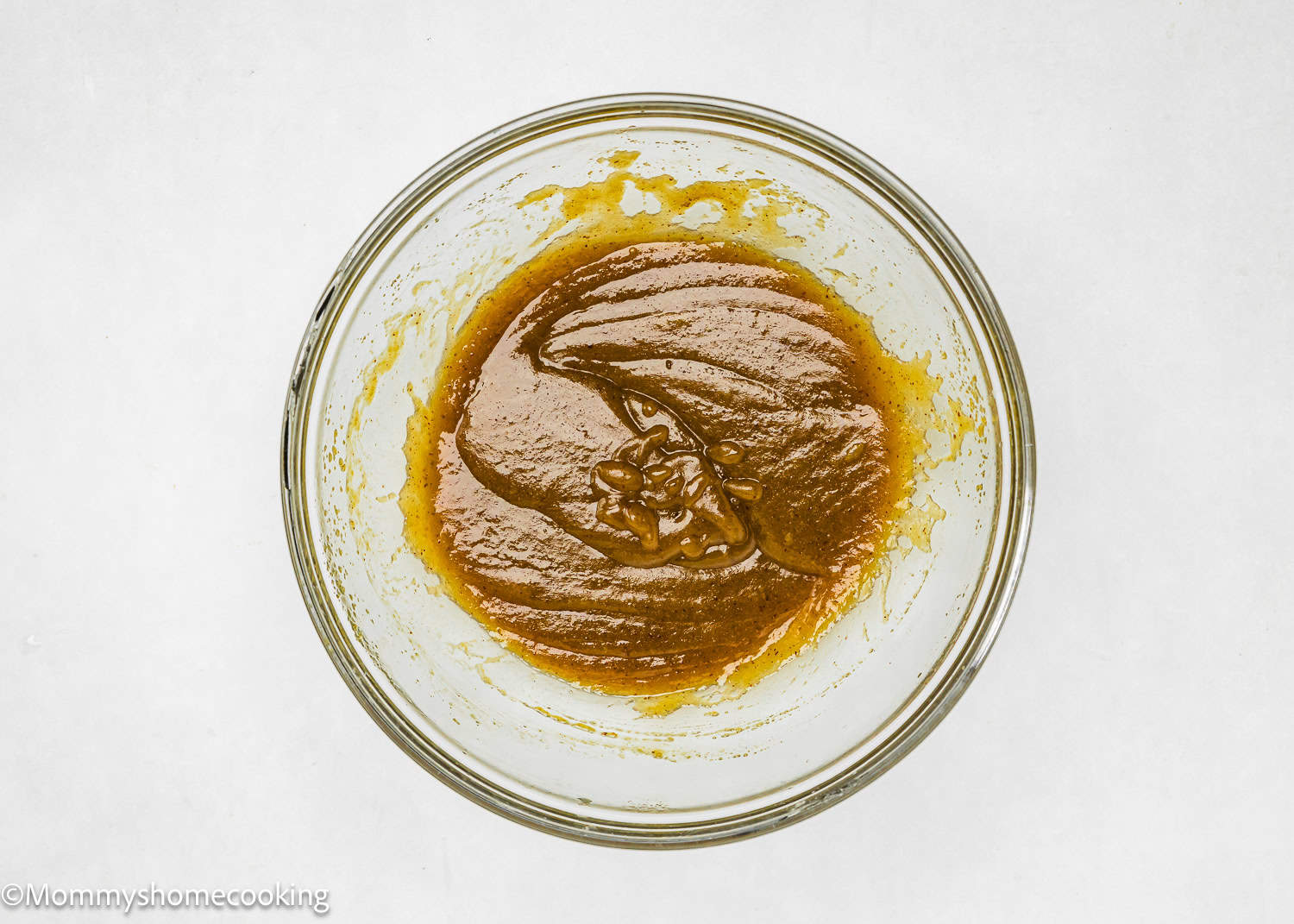 A single glass bowl is filled with wet ingredients mixture on a white background, reminiscent of the beginnings of easy-to-make eggless oatmeal raisin cookies.