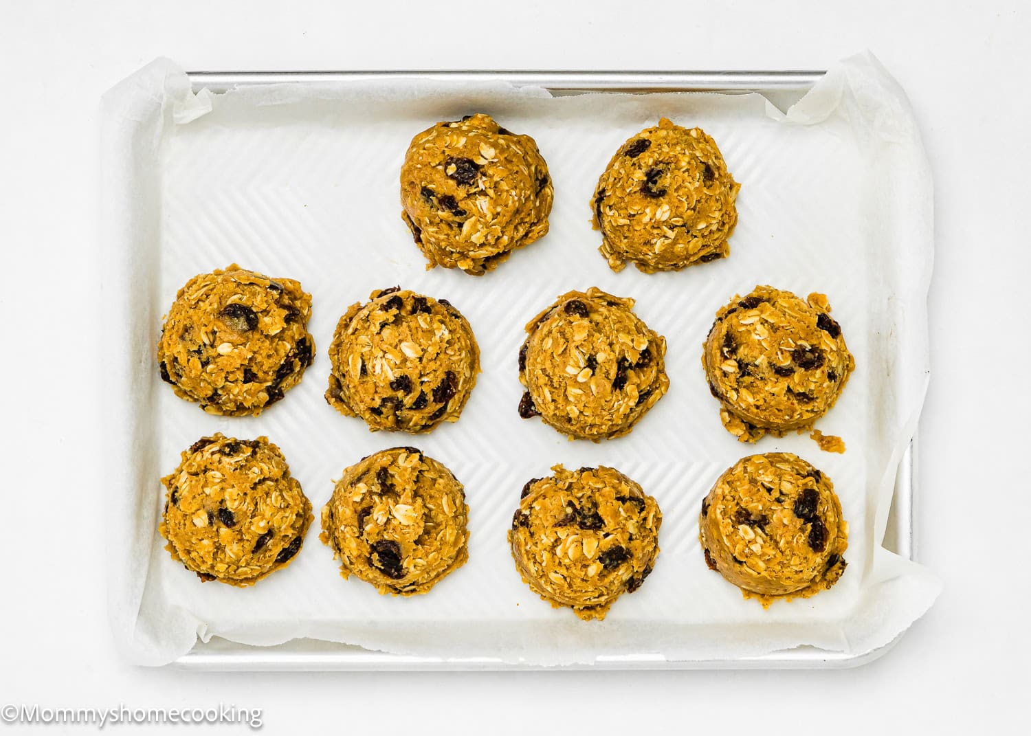 Ten eggless oatmeal raisin cookie dough balls rest on a parchment-lined baking sheet, showcasing an easy-to-make treat that requires just one bowl.