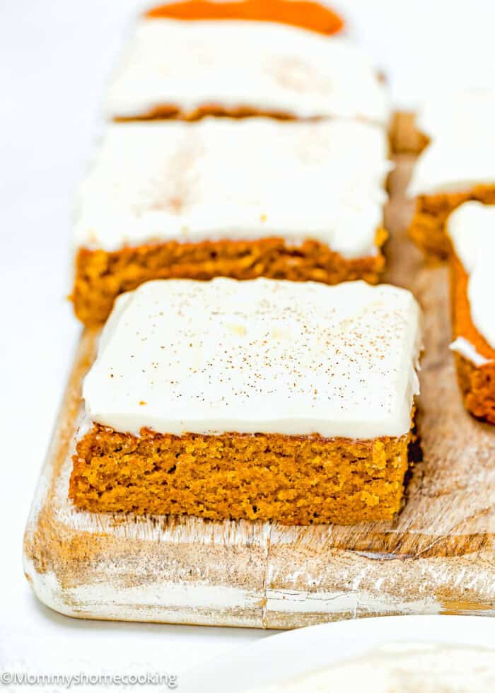 Eggless pumpkin bars topped with white frosting, sprinkled with cinnamon, and elegantly arranged on a wooden board.