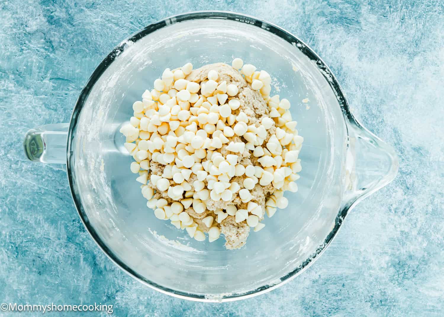 Eggless Cookie dough with white chocolate chips in a stand mixer bowl over a blue surface.