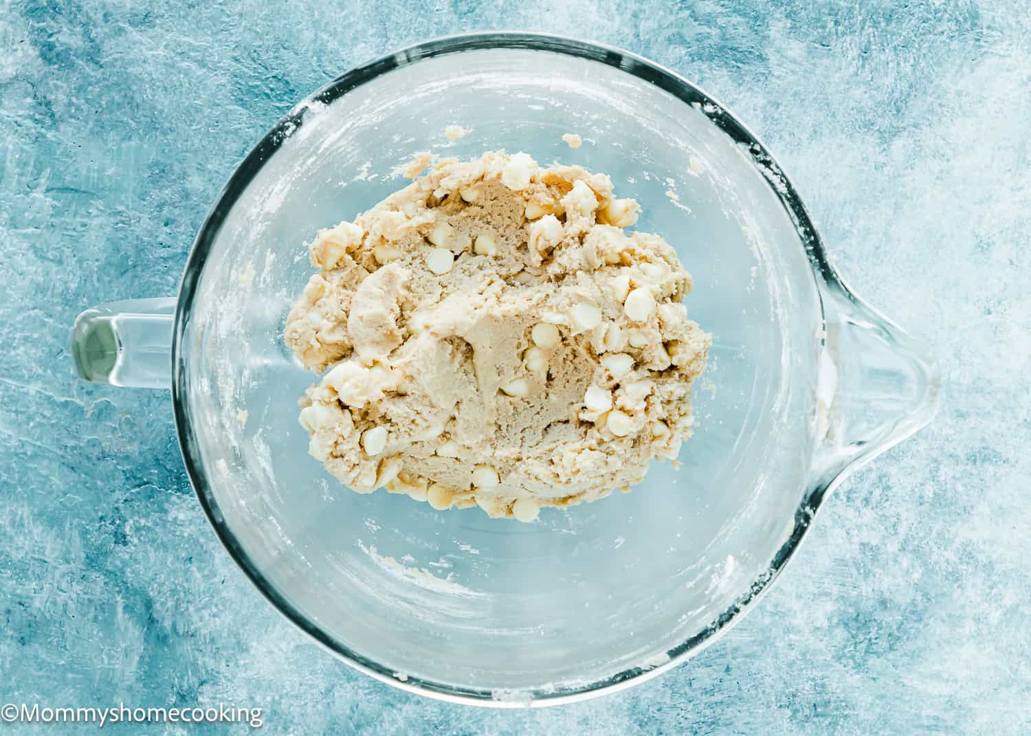 Eggless White Chocolate Cookie dough in a stand mixer bowl over a blue surface.