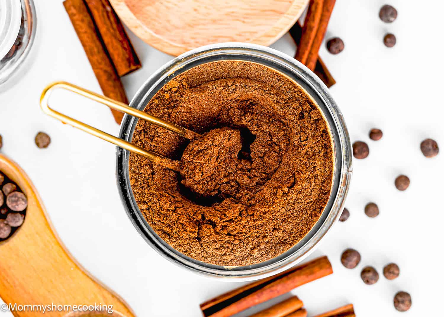 Overhead view of a jar filled with ground cinnamon, surrounded by cinnamon sticks and loose peppercorns, capturing the essence of a homemade pumpkin pie spice blend.