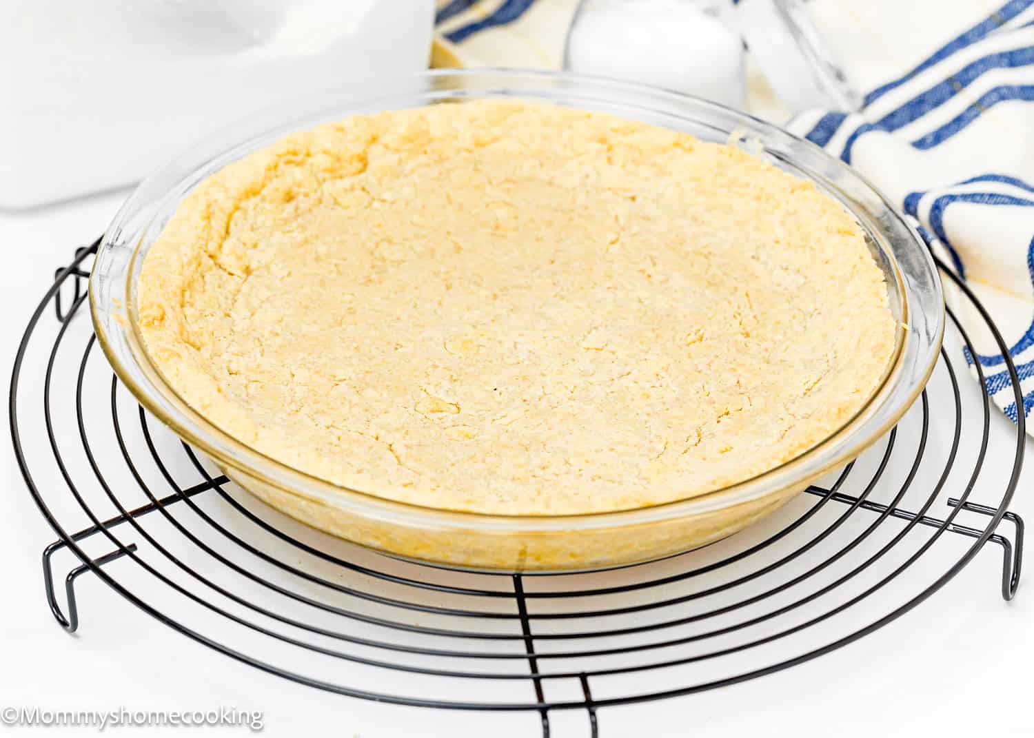 A quick, no-fuss pie crust is partially baked in a glass pie dish, resting on a cooling rack.