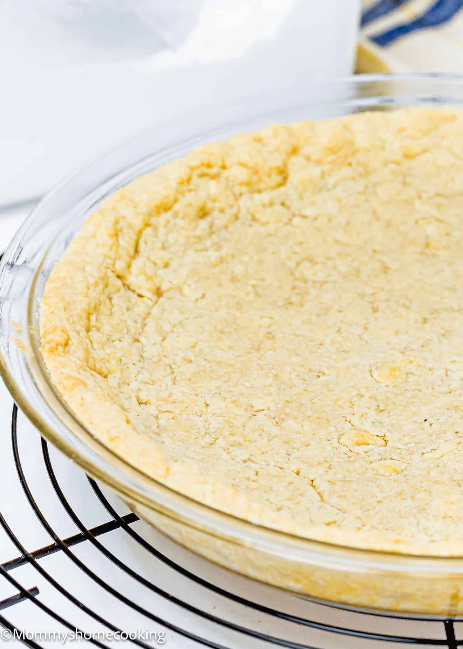 A clear glass pie dish with a baked, golden-brown crust from the Easy Press In Pie Crust recipe sits on a round cooling rack, effortlessly embodying a no-fuss and no chill baking experience.